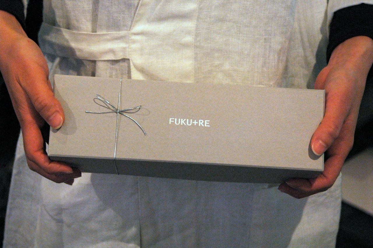 FUKU+REロゴ入りギフト箱を手に持つ様子。お礼やお返しに喜ばれる上品なお菓子ギフト。