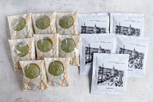 FUKU+RE(フクレ)のフクロウ最中のフロランタン8個と、100年前の籠島市街地の街並みが描かれたドリップコーヒー5袋の詰め合わせ。シンプルな背景の上に整然と並べられている