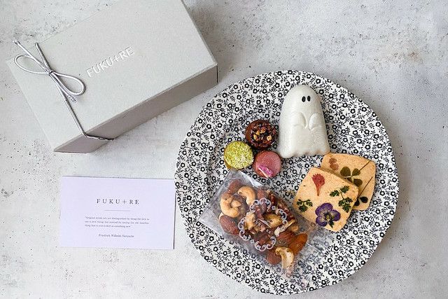 FUKU+REブランドのギフトボックスと、花の押し花クッキー、ナッツ、カラフルな焼き菓子、ゴースト型の和菓子を黒白模様の皿に盛り付けた上品なハロウィンスイーツセットの写真
