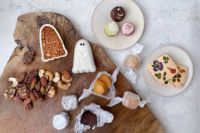 木製プレートに緑茶や紫芋の葛サブレ、桜島小みかんのアマレッティ、花やハーブが飾られた米粉サブレ、ゴースト型の最中スイーツ、ラム酒を使ったベイクドショコラ、ナッツを盛り付けた写真。見た目も可愛らしく、贈り物や配り用にも最適なハロウィンギフト。