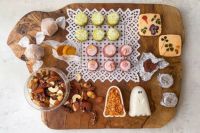 「おばけギフト（L）」のハロウィン限定スイーツが木製ボードに美しく並べられた写真。 緑茶や紫芋味のサブレの周りには、ナッツやゴースト型のフロランタン、エディブルフラワーとハーブがトッピングされた米粉サブレ、 キャラメル包みのアマレッティ、アルミで包まれたラム酒のベイクドショコラを配置しています。