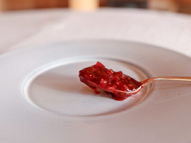 白い皿の上に置かれたスプーンに、粒感が際立つ鮮やかな赤色の果実ジャムがのっている。とろりと広がる艶のある質感が印象的に写されている。