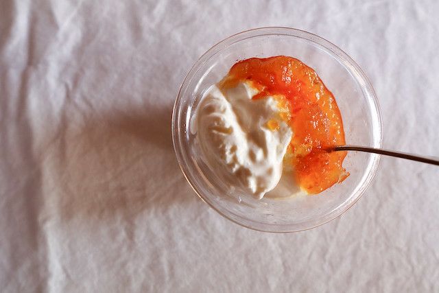 透明な器に盛られたヨーグルトに、橙色のジャムが添えられている。スプーンが添えられ、やわらかな光の中でデザートの質感が際立つ。